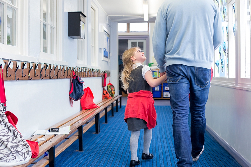 A photo of a dad walking his little girl down a school corridor