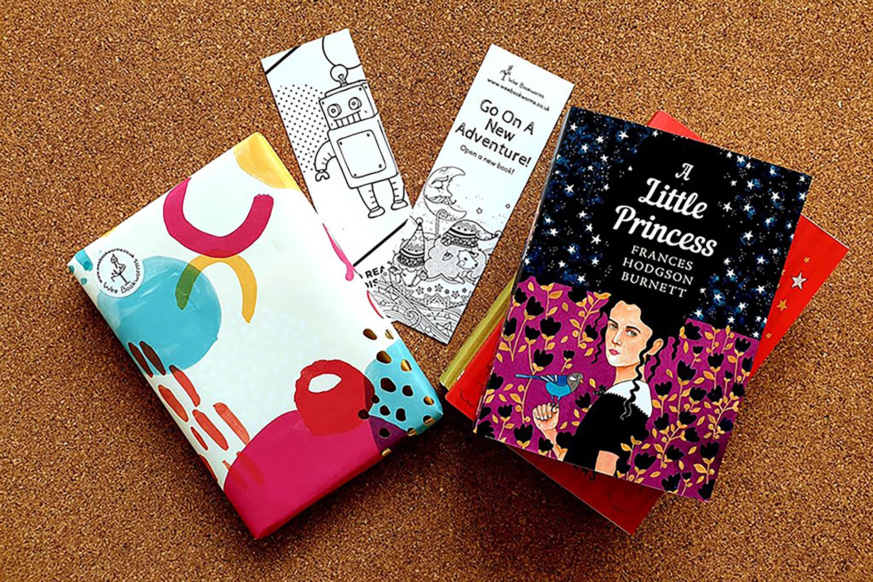 A photo of the contents of the Wee Bookworms subscription box.It includes a Puffin book, A Little Princess, next to a gift-wrapped book and some bookmarks on a carpet backdrop