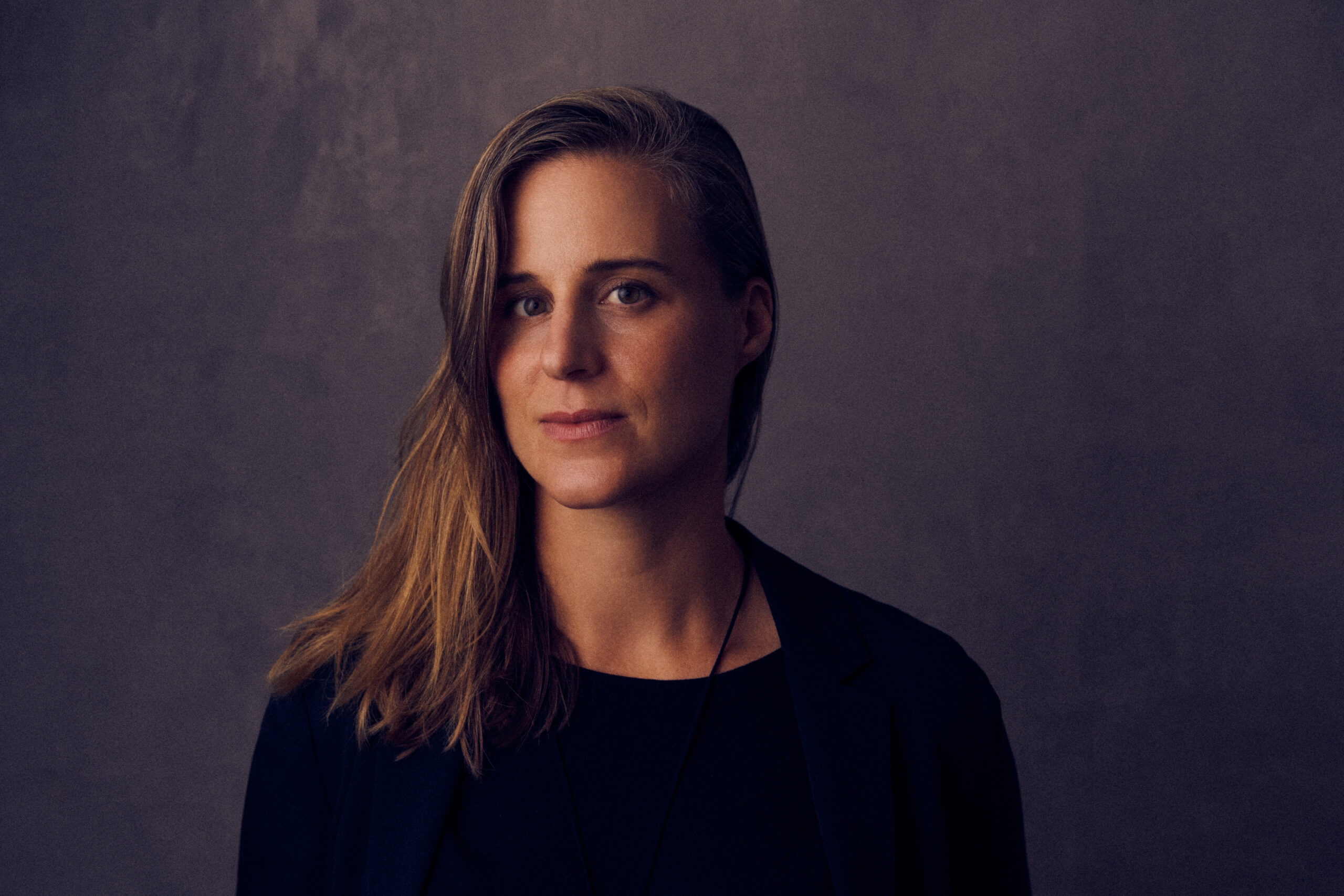 A dimly-lit photograph of Lauren Groff against a dark grey background