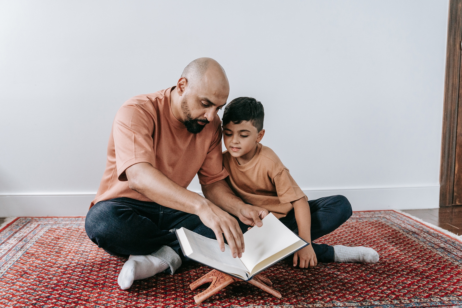 A photo of a father and son sitting on the floor reading the Qur'an toegther